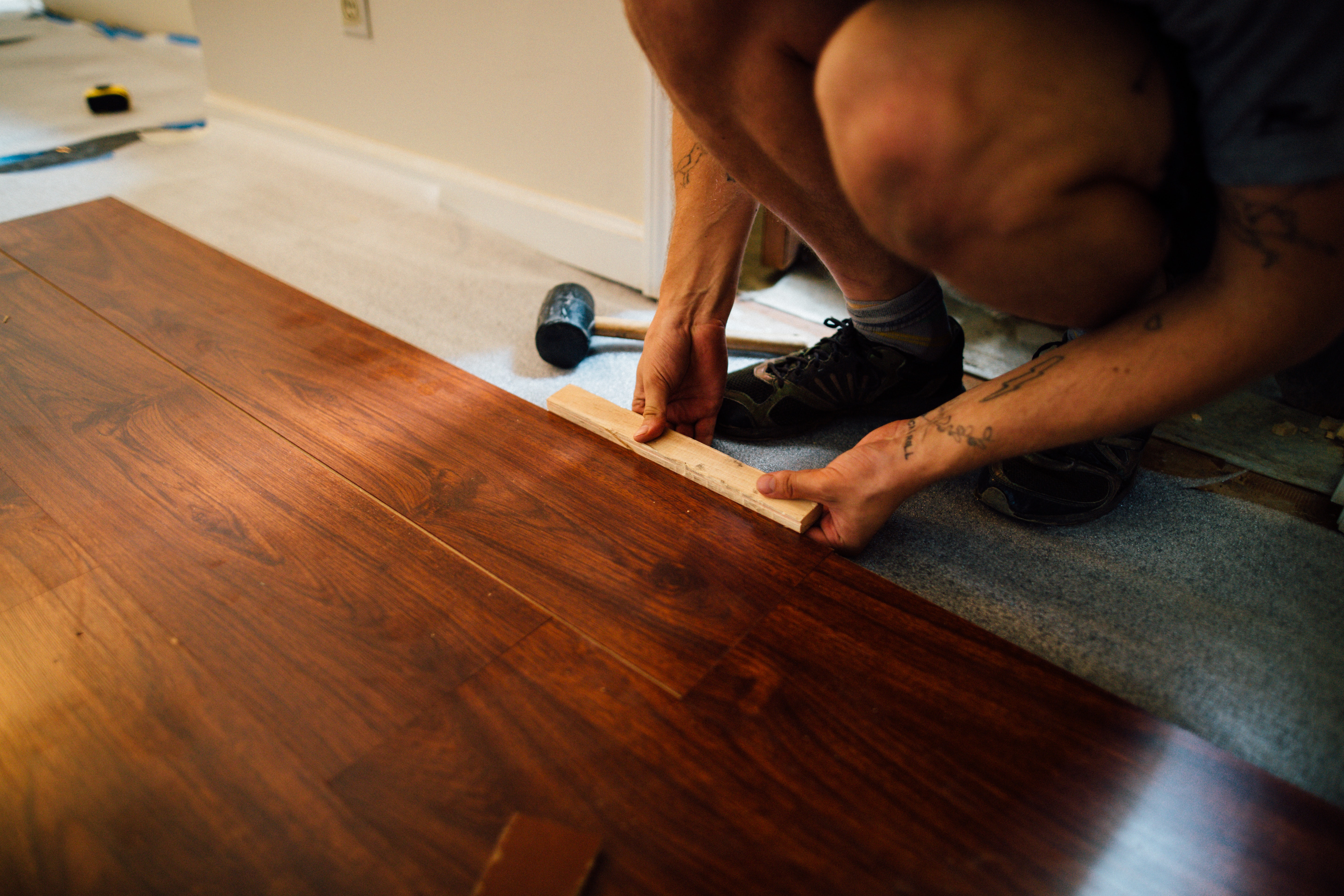 Stock photo of man leaning down to measure and install new hardwood flooring.